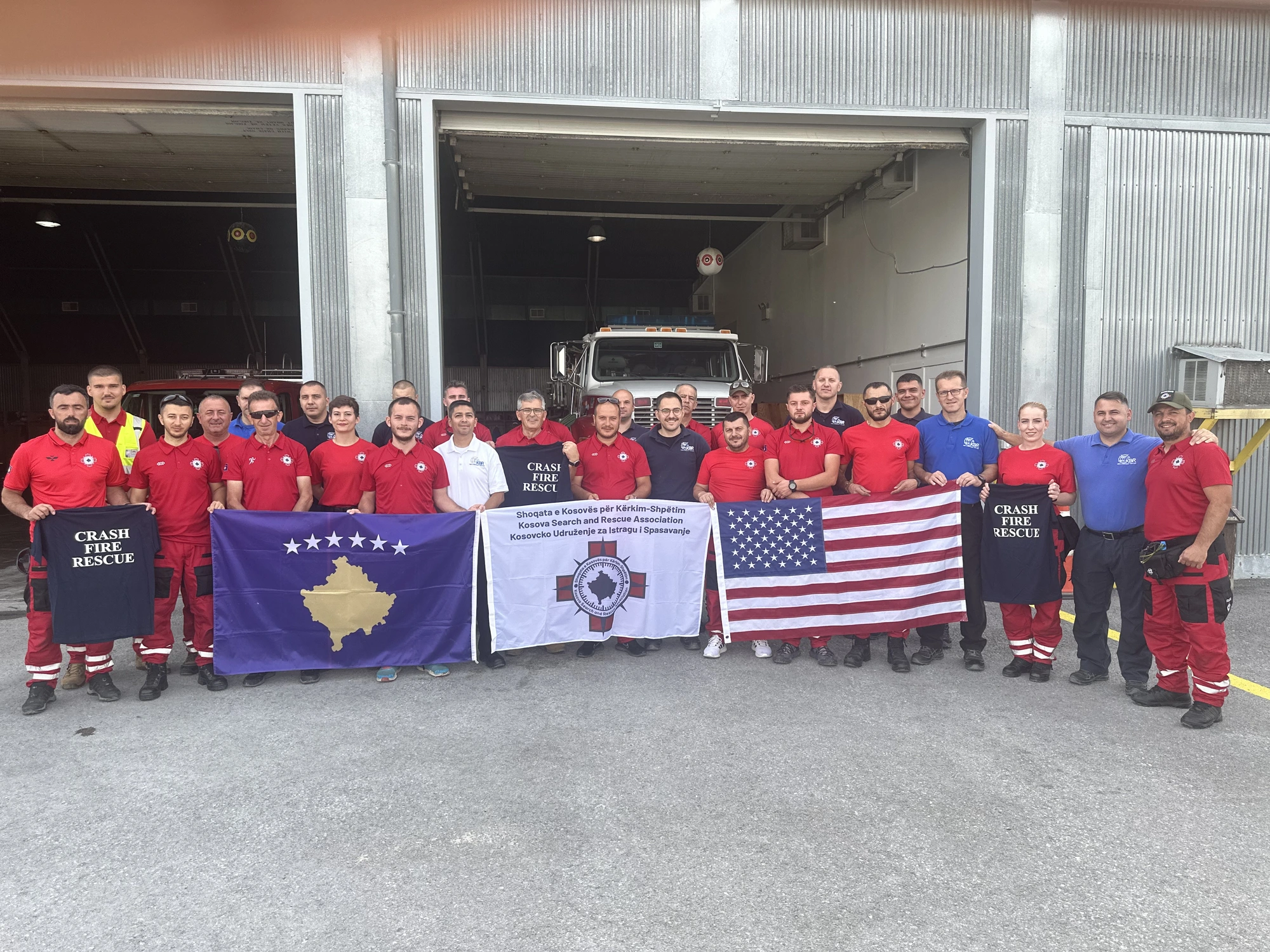 Group photo with Kosovo, KSRA and U.S. flags outside a Crash Fire Rescue bay