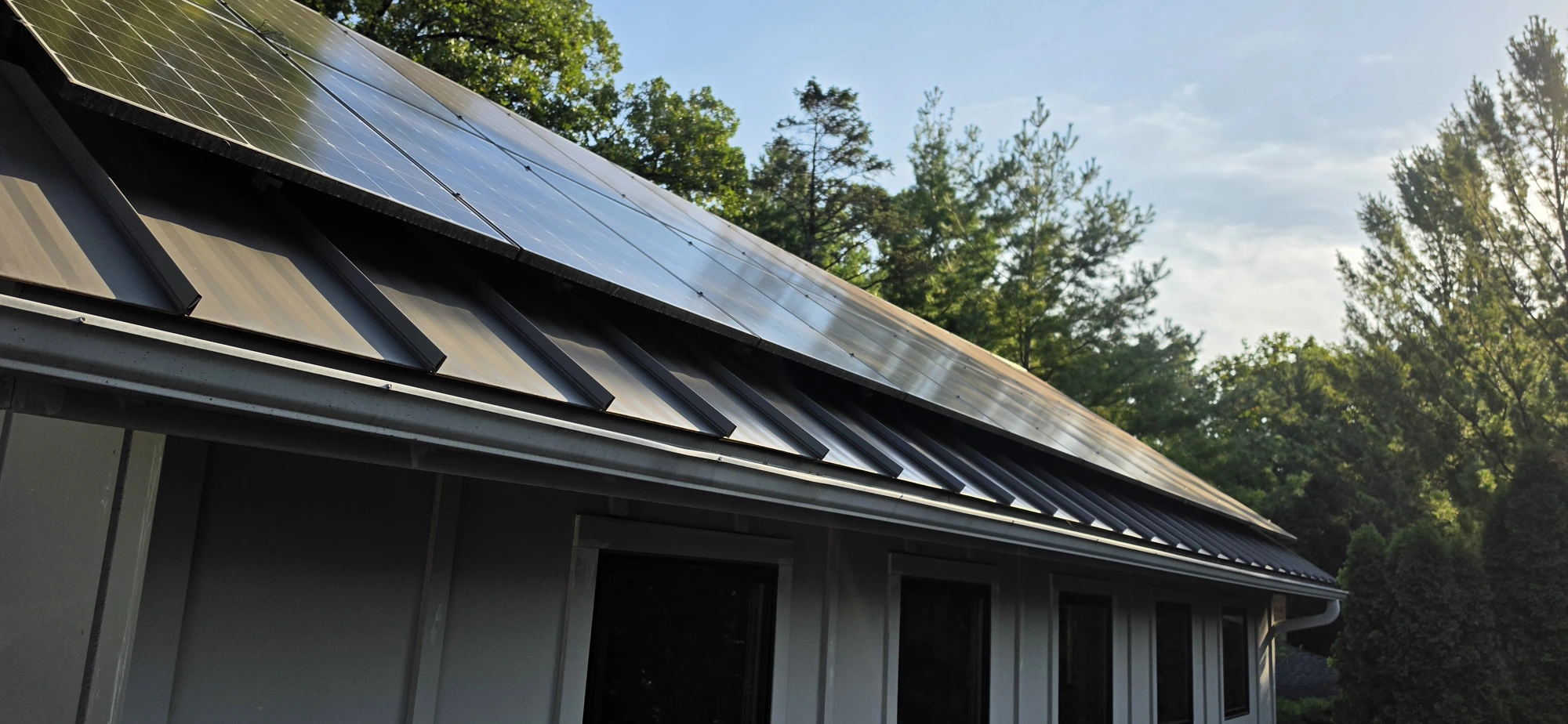 Southern Wisconsin residential solar array on a standing-seam metal roof photographed at 8:32 AM, showing a hazy dust and pollen film that dulls the panel glass and hides the underlying dark blue cells