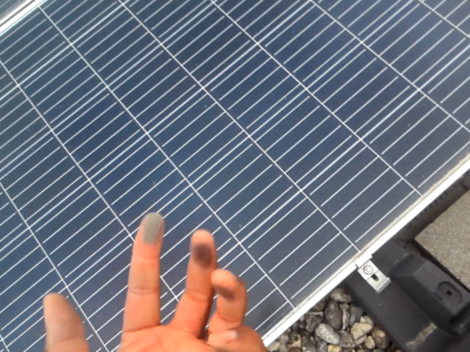 Marquis Mason performing the finger test on a commercial flat-roof solar panel — his fingertips are visibly blackened after a single swipe across the glass, revealing months of accumulated pollen, hard-water residue, and airborne particulate that were invisible from the ground