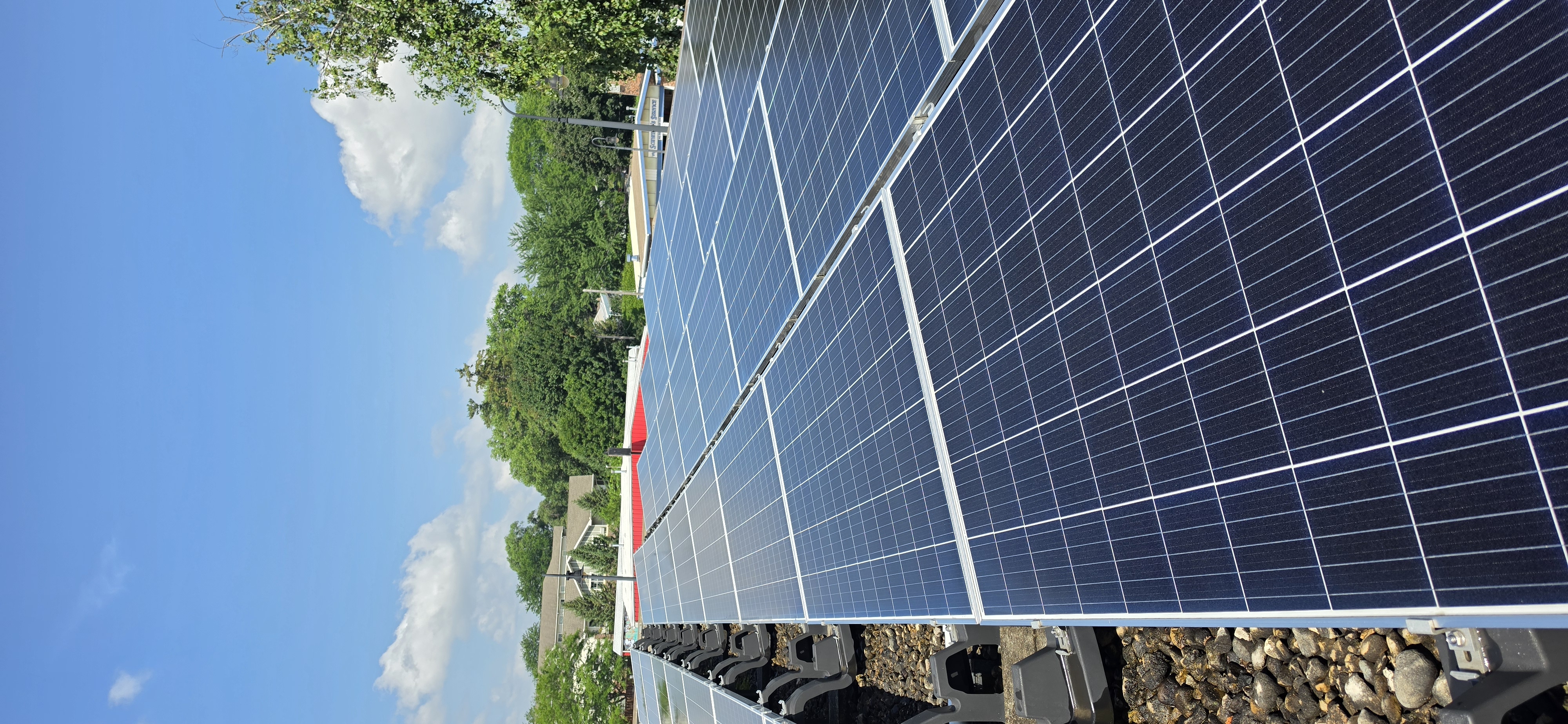 Same commercial array photographed under bright blue sky after cleaning — every panel returned to a rich uniform blue with the sky visibly reflected across the glass, framed by trees and the Southern Wisconsin skyline