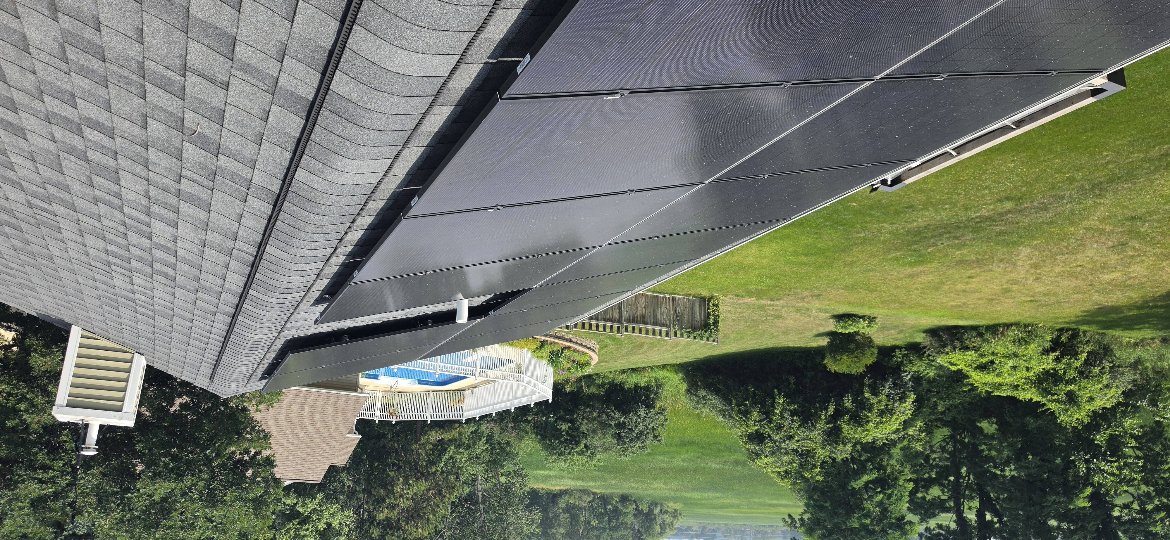 Residential rooftop solar array running along the ridge of a rural Southern Wisconsin home after a Solar Alchemist cleaning, with mature trees, a pool, and surrounding farm fields visible below