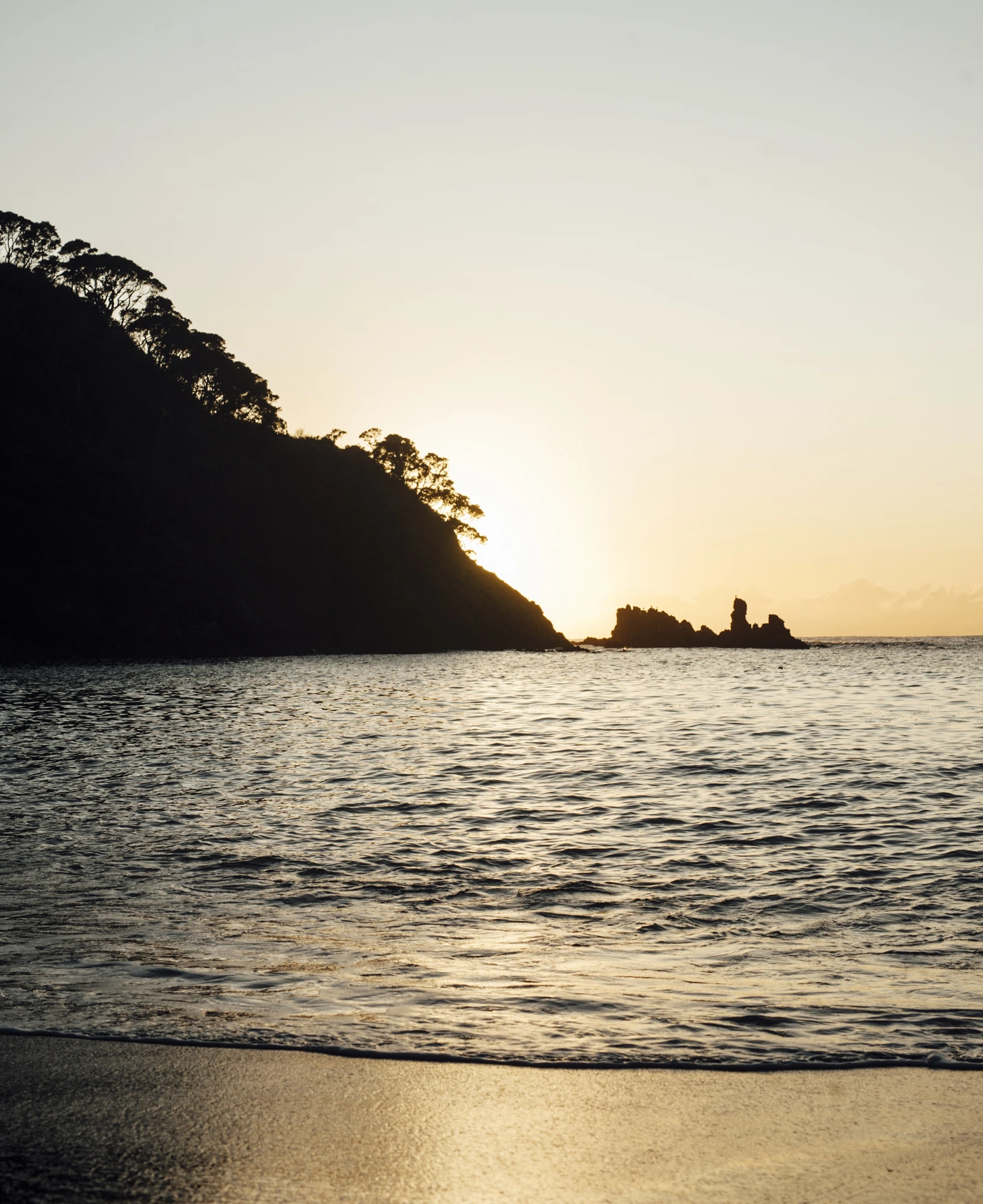 The sun setting over the ocean at Whananaki, a dark headland to the right