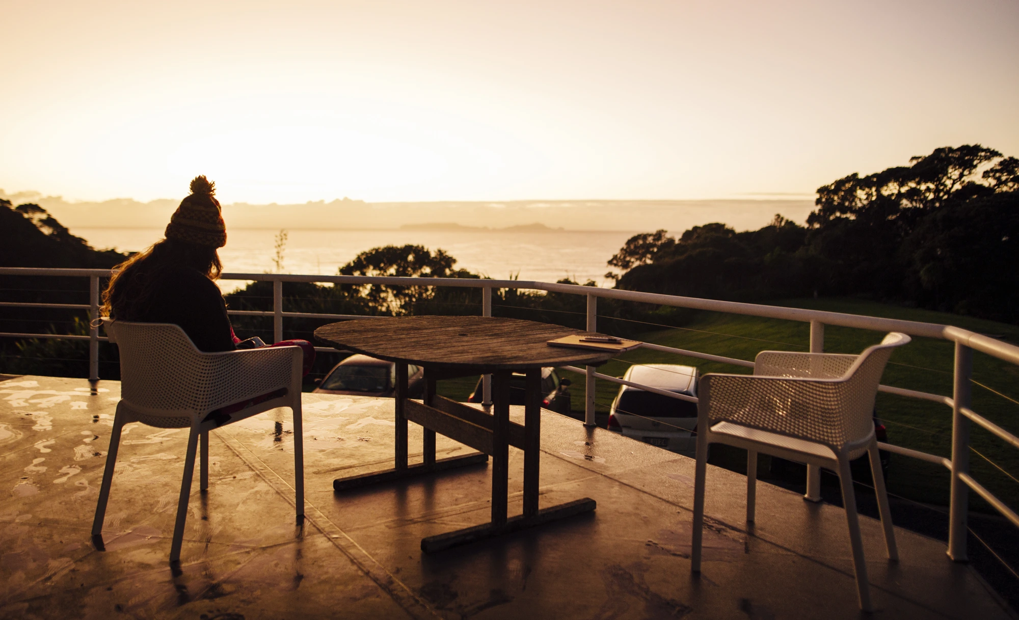 Someone sitting alone on a deck at sunset, looking out over the water